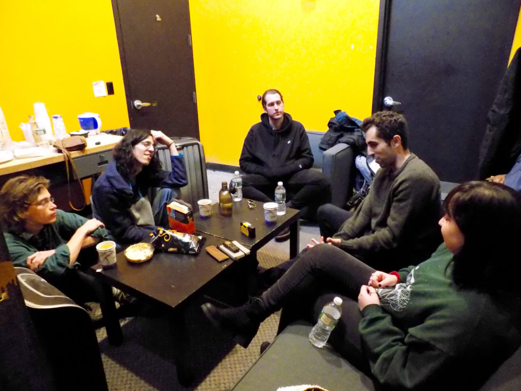 Four band members of Sure Sure sitting around a table in their green room talking to WCHC Station Manager, Hope